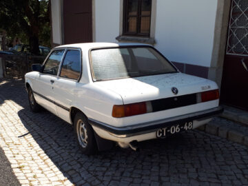 A white vintage BMW 316 is parked on a cobblestone street, with 