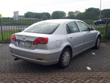 A silver Toyota sedan parked on a paved lot near a fence with a license plate reading 