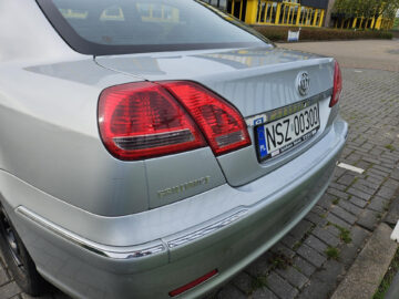 Rear view of a parked silver Brilliance BS4 sedan with Polish license plate NSZ 0300. The car's emblem reads 