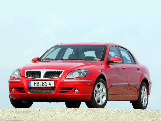 A red Brilliance BS4 sedan parked outside on a gravel surface, with a clear sky in the background. Spotted!