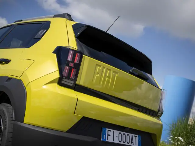 En un día soleado, un Fiat Grande Panda amarillo con detalles negros está aparcado en el exterior, con la vista trasera, incluidas las luces traseras, la matrícula y el logotipo de Fiat, claramente visibles.