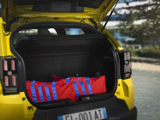 Le coffre ouvert d'une Fiat Grande Panda jaune contient deux sacs rouges et bleus, soulignant le caractère pratique de l'intérieur spacieux.