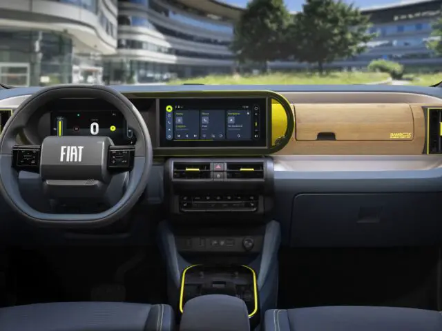 Innenraum eines Fiat Grande Panda mit einem modernen Armaturenbrett mit digitalen Anzeigen, einem Lenkrad mit Fiat-Logo und einem Materialmix aus Holz und Stoff.