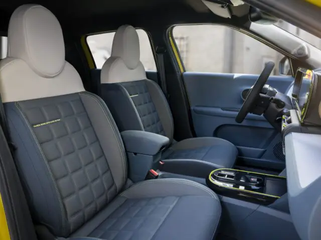 Vista interior de un Fiat Grande Panda moderno con dos asientos delanteros con tapicería acolchada, reposabrazos central y salpicadero visible con volante a la derecha. El meticuloso diseño del interior refleja la elegancia y la funcionalidad que los automovilistas buscan en los avanzados sistemas de propulsión actuales.