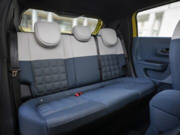 Interior trasero de un Fiat Grande Panda con asientos azules y grises con tapicería estampada, tres reposacabezas y cinturones de seguridad. La puerta del lado derecho está abierta, dejando al descubierto parte del asiento delantero azul.