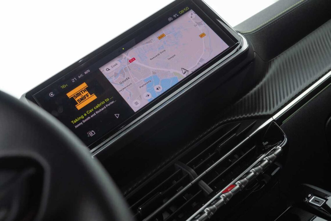 Close-up van het Peugeot 208 Hybrid-dashboard uit 2024 met een digitaal scherm met een navigatiekaart en een muziekspelerinterface. De kaart toont een stadsindeling met wegen, en de muziekspeler geeft een nummer en artiest aan. Dit model is al populair in Nederland.