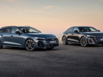 Twee strakke, moderne auto's, waaronder een elegante Audi A5, staan geparkeerd op een trottoir onder een zonsonderganghemel; de ene is een blauwe stationwagen en de andere een donkerblauwe sedan.