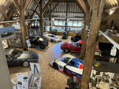 Een overdekte tentoonstelling toont vintage auto's, waaronder race- en klassieke modellen zoals die van Aston Martin, gerangschikt in een goed verlichte loft met houten balken en verschillende informatieborden en memorabilia van de Heritage Trust.