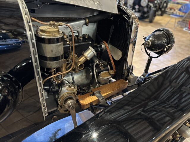 A close-up of the engine compartment of an antique Aston Martin, showing various mechanical components, pipes and wiring in a vintage vehicle. This detailed image could easily belong in the Heritage Trust Museum's PHOTORAGE collection.