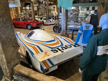 Several vintage race cars are on display at the Heritage Trust Museum, including a white car with a blue, yellow and red stripe color scheme in the foreground. In the background, visitors can admire a historic formula car and an Aston Martin beautifully captured in this photo essay.