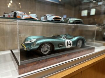 In het Heritage Trust Museum staat een vitrine met gedetailleerde schaalmodellen van klassieke raceauto's, waaronder een Aston Martin en een groene auto met nummer 14 op de voorgrond, waarmee de geschiedenis wordt vastgelegd als in een fotoreportage.