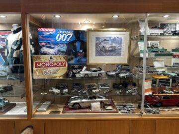 Een vitrine in het museum met verschillende James Bond-memorabilia, waaronder schaalmodellen van auto's van de Aston Martin Heritage Trust, bordspellen, een ingelijste foto en andere thema-verzamelobjecten.