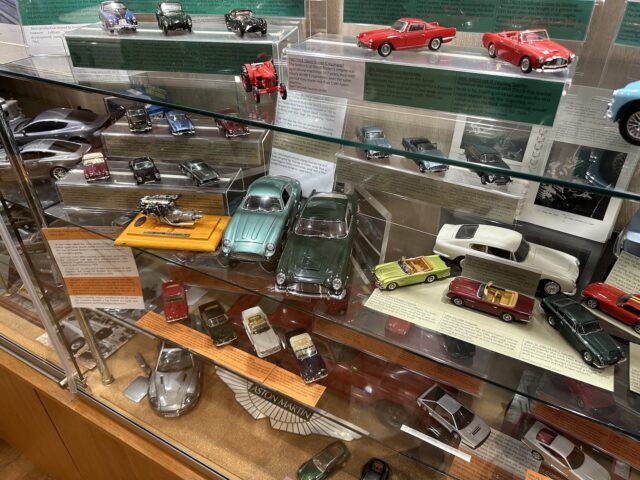 A display case at the Heritage Trust Museum contains a variety of model cars, including vintage and modern designs. The shelves are filled with meticulously detailed Aston Martin miniatures in a variety of colors and styles, offering a fascinating photographic record of automotive history.