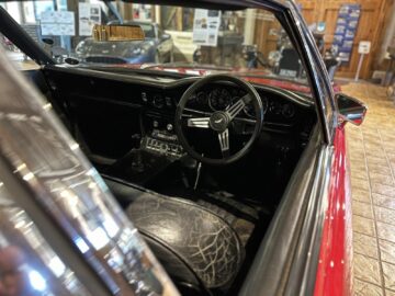 Interior view of a red classic convertible with a black leather steering wheel, dashboard with dials and gauges and black leather seats, reminiscent of an exhibit you might find at the Heritage Trust Museum.