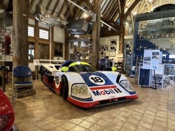 En el Museo Heritage Trust se expone un coche de carreras con el número 18 y el logotipo de Mobil 1, rodeado de recuerdos y trofeos automovilísticos, creando un fascinante registro fotográfico de la historia de las carreras.