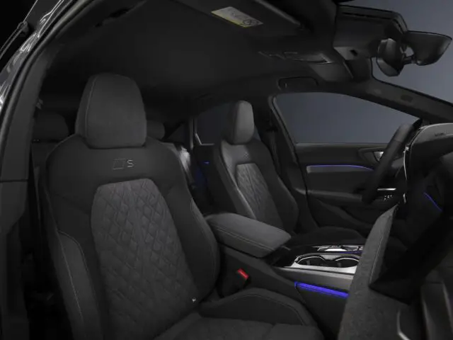 Het interieur van de Audi A5 omvat de voorstoelen met zwarte stoffen bekleding, een middenconsole en een dashboard met scherm. Blauwe sfeerverlichting accentueert het verfijnde interieur.