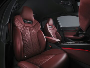 The image shows the front interior of an Audi A5 with two seats. The seats are upholstered in dark red leather with a diamond stitch pattern. The dashboard and door also feature matching red accents.