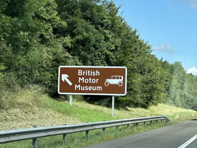 Een verkeersbord op een snelweg geeft de richting aan naar het British Motor Museum, met een illustratie van een auto, perfect voor degenen die een bezoek plannen om de uitgebreide collectie te verkennen.