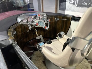 Het interieur van een klassieke auto in het British Motor Museum toont een futuristisch dashboard met analoge meters, een houten paneel en een witleren stoel met aluminium accenten; het is een elegante tentoonstelling die elke bezoekersreportage waardig is.