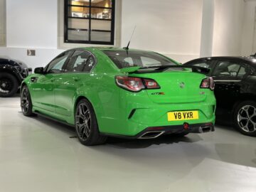 Een felgroene sportsedan met een achterspoiler, met het opschrift "GTS-R" en met het kenteken "V8 VXR", staat binnen geparkeerd bij het British Motor Museum.