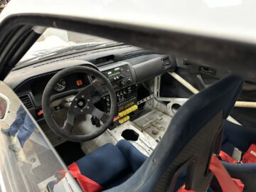 De uitgeklede cockpit van de rallyauto is voorzien van een zwart stuur, een uitgebreid bedieningspaneel met diverse schakelaars en knoppen, blauwe racestoelen en rode veiligheidsgordels. Als u dergelijke precisietechniek van dichterbij wilt bekijken, kunt u uw bezoek aan het British Motor Museum plannen voor een diepgaande reportage over de autogeschiedenis.