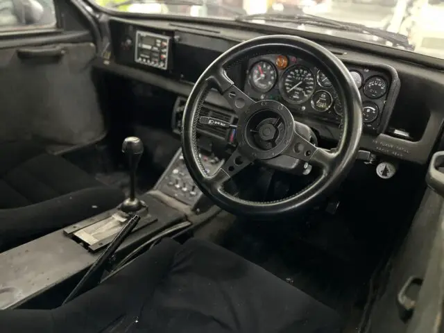 Close-up van het interieur van een oldtimer in het British Motor Museum, met het stuur, het dashboard met meters, de handmatige versnellingspook en de bestuurders- en passagiersstoelen. Perfect voor elke reportage waarin klassiek auto-ontwerp wordt vastgelegd.