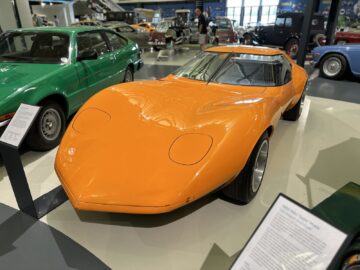 Een oranje, aerodynamische vintage sportwagen staat centraal in het British Motor Museum. Gedetailleerde informatieborden staan voor elk klassiek voertuigmodel en bieden bezoekers een uitgebreid bij-de-bezoek.