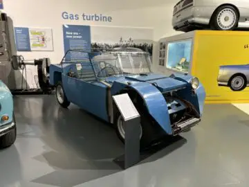 Een blauwe, onvolledige prototype-auto tentoongesteld in het British Motor Museum, aangegeven met informatie over de "gasturbine" -technologie. De auto mist een afgewerkte carrosserie en heeft zichtbare mechanische componenten.