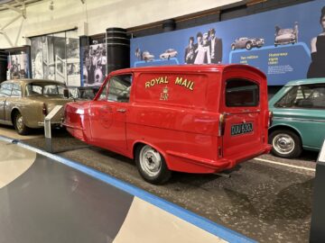 Een rood Royal Mail-busje met de registratie DUU 630D wordt tentoongesteld in het British Motor Museum, omringd door andere oldtimers en informatieve displays aan de muur. De tentoonstelling biedt bij elk bezoek een nostalgische kijk op de transportgeschiedenis.