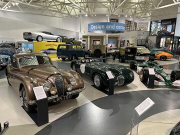 Een bezoek in reportagestijl aan het British Motor Museum onthult een verzameling vintage en klassieke auto's die worden tentoongesteld in een overdekt automuseum, met op de achtergrond een tentoonstellingsbord met de tekst "Design and Concept".