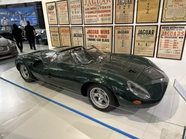 In het British Motor Museum staat een donkergroene vintage Jaguar-sportwagen tentoongesteld, omringd door historische posters en informatie over de prestaties van het merk, waardoor het een must-visit is voor elke autoliefhebber.