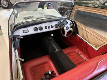 Interieur van een vintage cabriolet met rode en zwarte stoelen, een eenvoudig dashboard met draaiknoppen, een stuur en een versnellingspook: perfect voor elk bezoek aan het British Motor Museum.