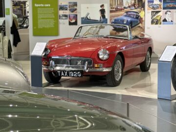 Een rode vintage cabrioletsportwagen met kenteken 'TAX 192G' wordt tentoongesteld in een tentoonstelling over sportwagens in het British Motor Museum en trekt bezoekers en liefhebbers.