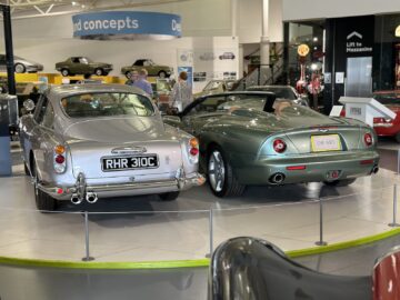 Twee vintage Aston Martin-auto's, een zilveren coupé (kentekenplaat RHR 310C) en een groene cabriolet (kentekenplaat DB AR1), zijn te zien in het British Motor Museum. Omringd door andere auto's en tentoonstellingsstukken trekt hun tijdloze elegantie de aandacht van elk bezoek.