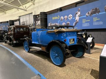 In het British Motor Museum staat een blauwe vintage auto tentoongesteld. Op het kenteken staat "SD 8284". Op de muur erachter hangen informatiedisplays met afbeeldingen en tekst uit de jaren dertig, waardoor bij elk bezoek een ware reis door de tijd wordt gemaakt.