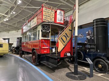 Een vintage rode dubbeldekkerbus tentoongesteld in het British Motor Museum, voorzien van advertenties en route-informatie met nummer 36 en kenteken XM 7399, is een hoogtepunt voor elk bezoek.