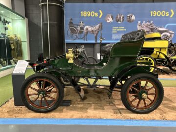 In het British Motor Museum is een groene vintage auto met houten wielen te zien, naast een tijdlijntentoonstelling met voertuigen uit de jaren 1890 en 1900. Plan vandaag nog uw bezoek voor een meeslepende reis door de autogeschiedenis.