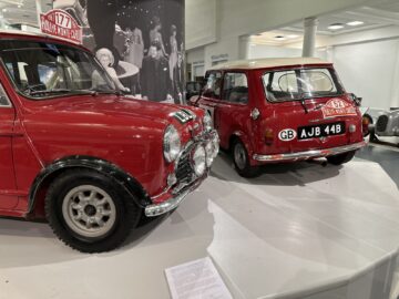 In het British Motor Museum zijn twee rode Mini Coopers met rallynummers te zien, met een goed bewaard gebleven exterieur en historische informatieborden. Zwart-witfoto's op de achtergrond zorgen voor een nostalgische reportage voor bezoekers.