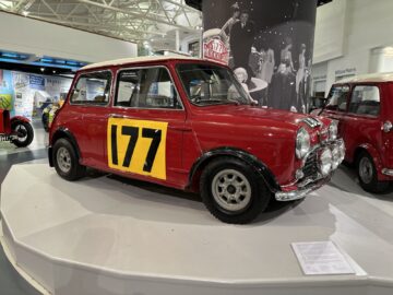 Een rode klassieke auto met het nummer 177 op de zijkant, gelegen op een wit platform in het British Motor Museum. Ideaal voor wie een bezoek plant of een autoreportage schrijft.