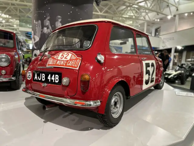 Een rode vintage mini-raceauto, genummerd 52 en voorzien van kenteken AJB 44B, is te zien in de overdekte tentoonstelling van het British Motor Museum, wat een ideaal bezoek en perfect is voor een nostalgische reportage.