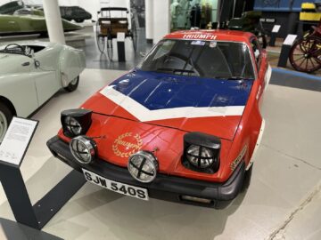 In een boeiende reportage in het British Motor Museum wordt een klassieke Britse sportwagen in de kleuren rood, wit en blauw getoond. De auto is voorzien van vier aan de voorzijde gemonteerde rallylampen en er staat "Triumph" op de motorkap. Een must-see voor elk bezoek aan dit iconische instituut.