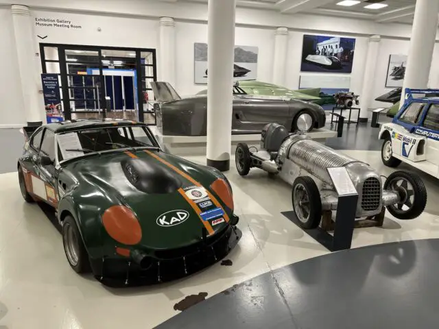 Een foto van raceauto's in het British Motor Museum. De reportage legt de gestroomlijnde voertuigen vast die elegant op de vloer zijn geplaatst, met pilaren en informatieborden die context op de achtergrond bieden.