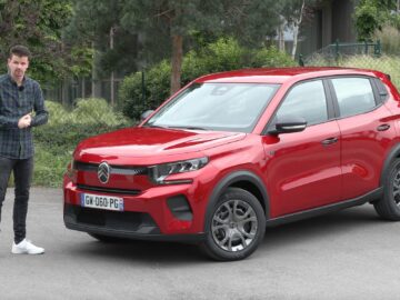 Bart Oostvogels staat naast een rode SUV die op een betonnen ondergrond geparkeerd staat en toont de indrukwekkende uitrusting Citroën C3, met bomen en groen op de achtergrond.