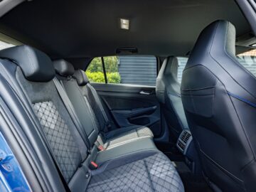 The interior of a VW Golf, shown from the rear seat perspective, with black leather seats with diamond stitching, a center armrest and the back of the front seats.