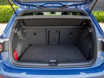 Open trunk of a blue VW Golf with a spacious, empty cargo area with gray carpet and a folded down rear seat.