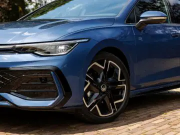 Front view of a blue VW Golf parked on a paved lot, highlighting the left headlight, grille and alloy wheels.