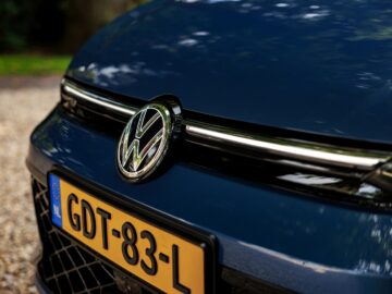 Close-up van de voorkant van een blauwe VW Golf met een kentekenplaat met de tekst "GDT-83-L", geparkeerd op een grindoppervlak.