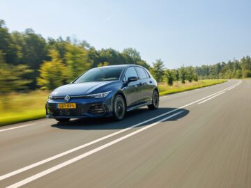 Een VW Golf in levendig blauw rijdt langs een zonnige, met bomen omzoomde landelijke weg.