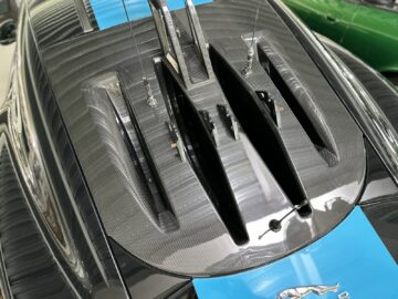 Close-up of the hood of a car with carbon fiber details and two large air intakes, with a blue stripe and metal Mustang emblem, as seen in the Jaguar Heritage Trust Collection.