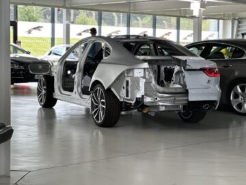 A partially assembled silver car chassis, part of the Jaguar Heritage Trust Collection, in a car factory, with internal structures visible; a true example of industrial reportage.